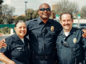 Three police officers smiling and posing in an outdoor setting, showcasing camaraderie in law enforcement.
